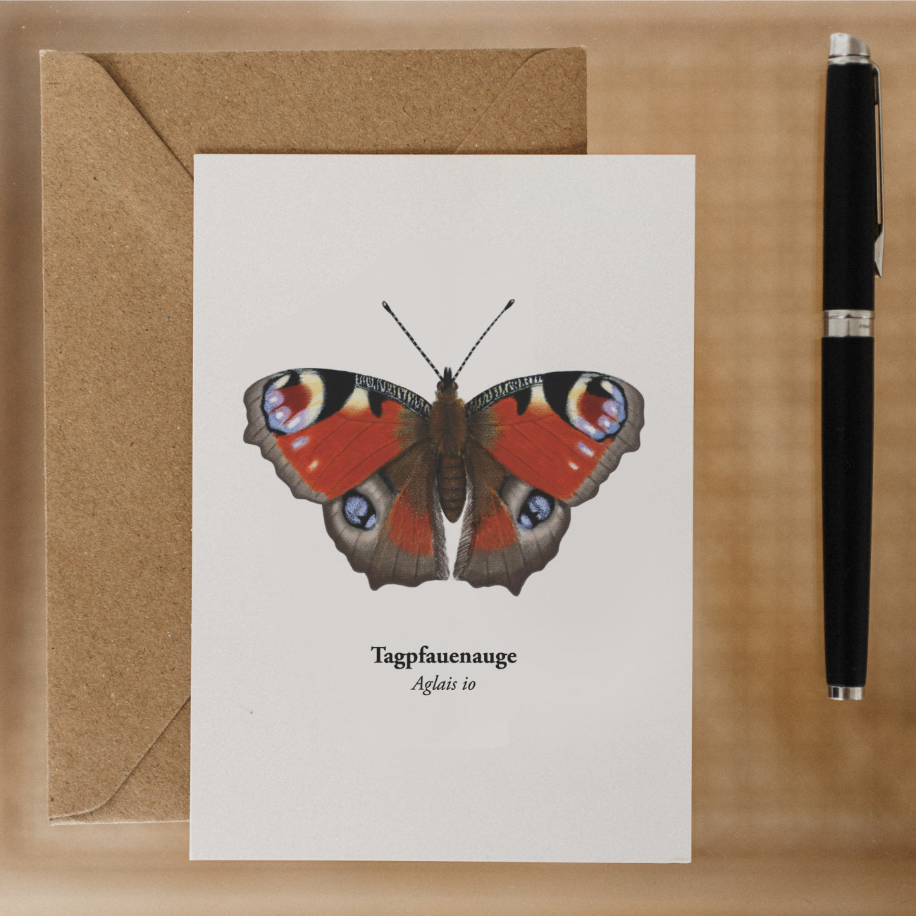 Postkarte mit Tagpfauenauge und Recyclingumschlag neben Stift – zum Verschenken