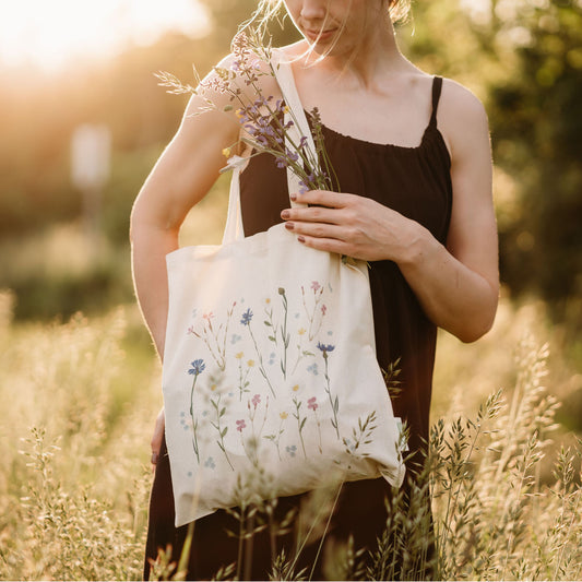 Person trägt eine Stofftasche mit Wildblumen-Print in sommerlicher Wiese