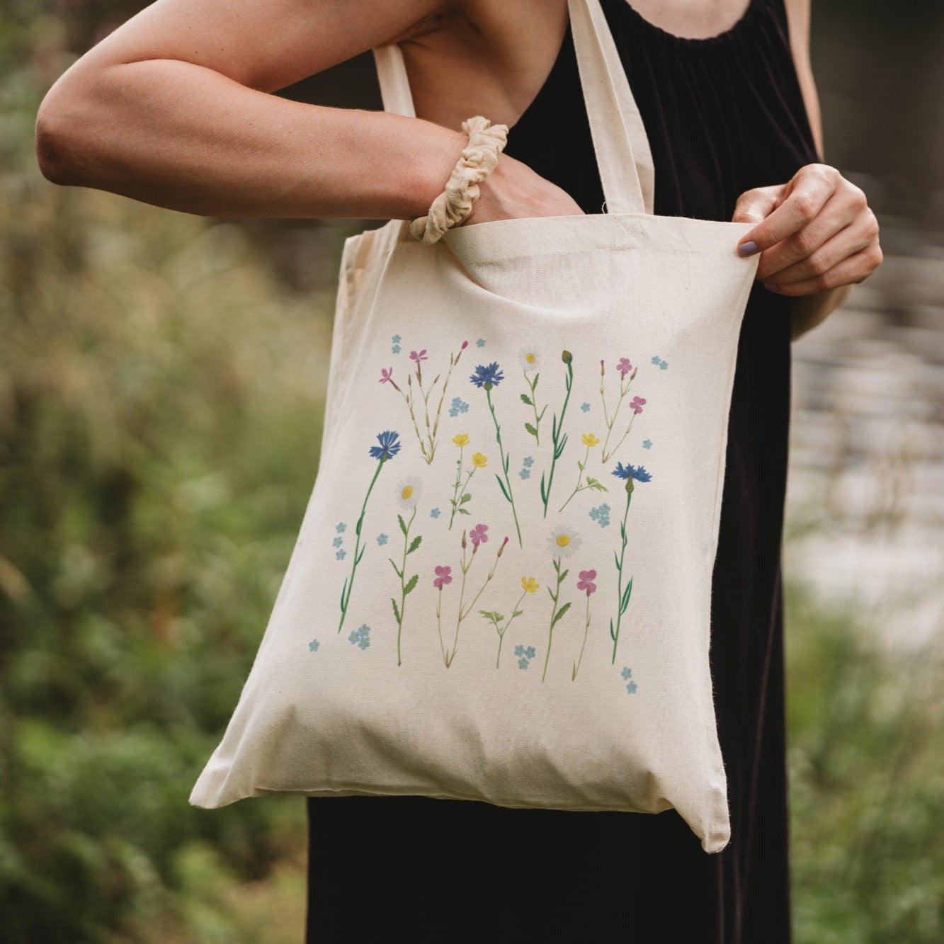 Stofftasche mit Wildblumen-Motiv in der Hand, vor Naturkulisse