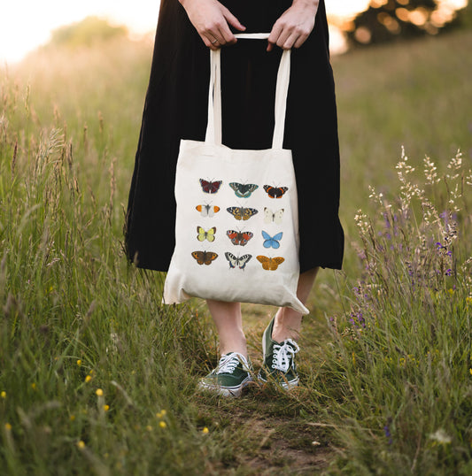 Schmetterling Baumwolltasche – Frau trägt Stofftasche mit Schmetterlingsillustration und Wildblumen im Sonnenuntergang