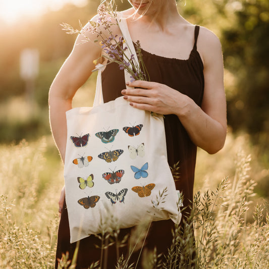 Schmetterling Stofftasche aus Baumwolle – Frau hält Tasche mit 12 heimischen Schmetterlingsarten auf sommerlicher Wiese